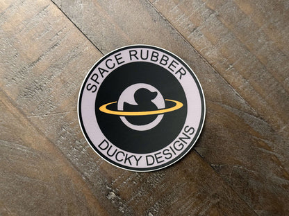 Space Rubber Ducky Designs decal sticker. 3" circle die cut vinyl decal. Matte finish and weather resistant. Features the company logo. 