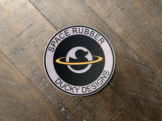 Space Rubber Ducky Designs decal sticker. 3" circle die cut vinyl decal. Matte finish and weather resistant. Features the company logo. 