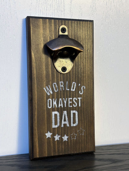 Custom magnetic bottle opener featuring a "World's Okayest Dad" theme. Each bottle opener is handmade and has hidden rare earth magnets to catch metal bottle caps. Wall-mounted or magnetic backing options. Made by Space Rubber Ducky Designs in Southern California, USA.