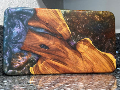 The natural beauty of this live edge mesquite serving board is accented with a blast of color.  Dark blues and purples swirl together like a galactic nebula while a bubbling sea of color hypnotizes.   Food safe epoxy resin was used to create this design. Using knives or other sharp utensils on the epoxy resin surface may damage it and is not recommended.  Board dimensions:  17"L x 9.75"W x 0.75"H.  As a handcrafted product, please allow for approximately 1/4" variation in dimensions.