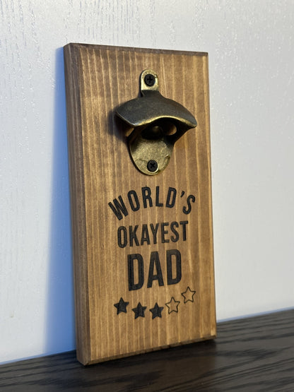 Custom magnetic bottle opener featuring a "World's Okayest Dad" theme. Each bottle opener is handmade and has hidden rare earth magnets to catch metal bottle caps. Wall-mounted or magnetic backing options. Made by Space Rubber Ducky Designs in Southern California, USA.