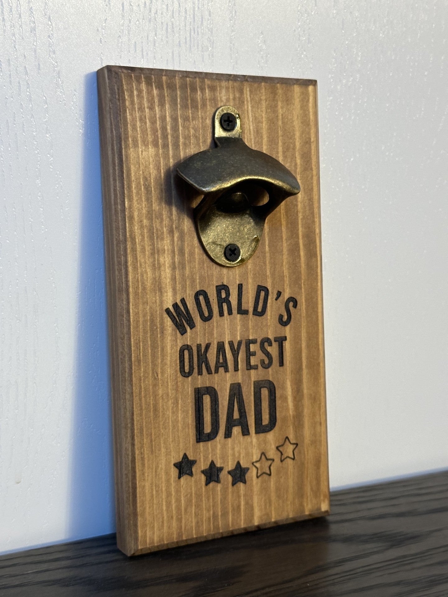Custom magnetic bottle opener featuring a "World's Okayest Dad" theme. Each bottle opener is handmade and has hidden rare earth magnets to catch metal bottle caps. Wall-mounted or magnetic backing options. Made by Space Rubber Ducky Designs in Southern California, USA.